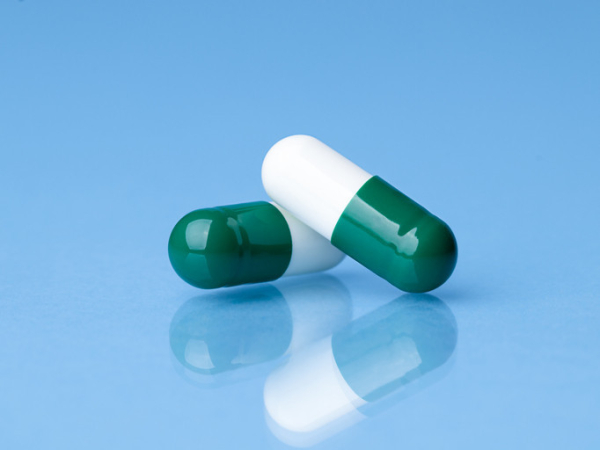 Two identical green and white capsules against a blue background; one may be active medicine while the other may be placebo